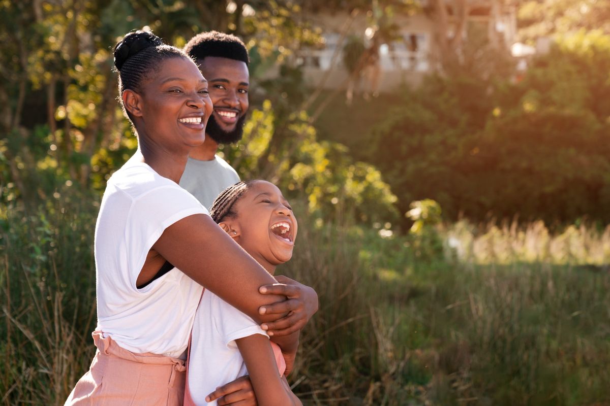 A family of three laughing together outdoors in golden light